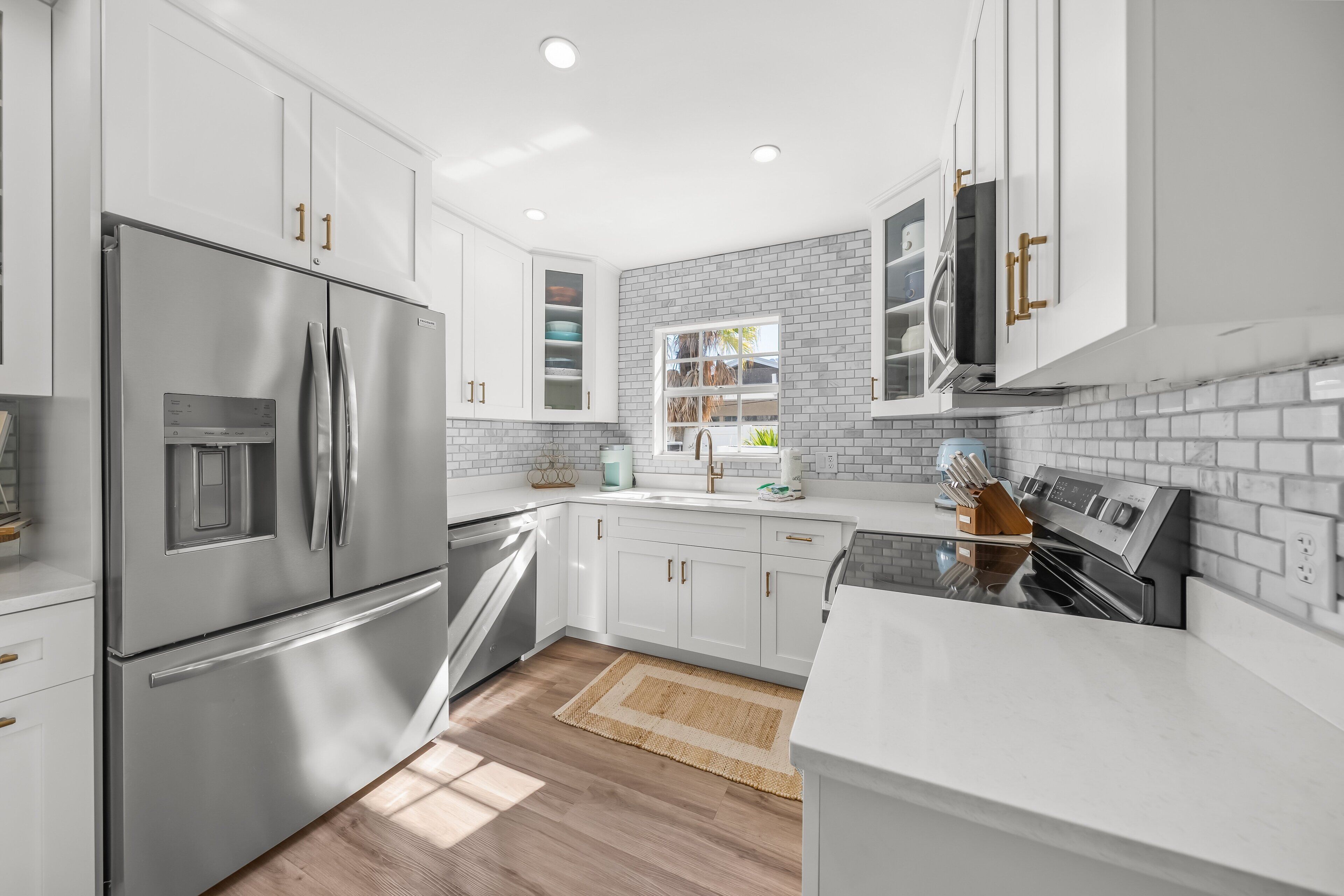 Una cucina moderna con mobili bianchi, elettrodomestici in acciaio inossidabile e una finestra che illumina naturalmente l'ambiente.