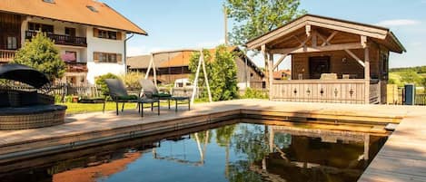 Una piscina con muelle de madera, una zona de estar cubierta y un edificio con techo inclinado.