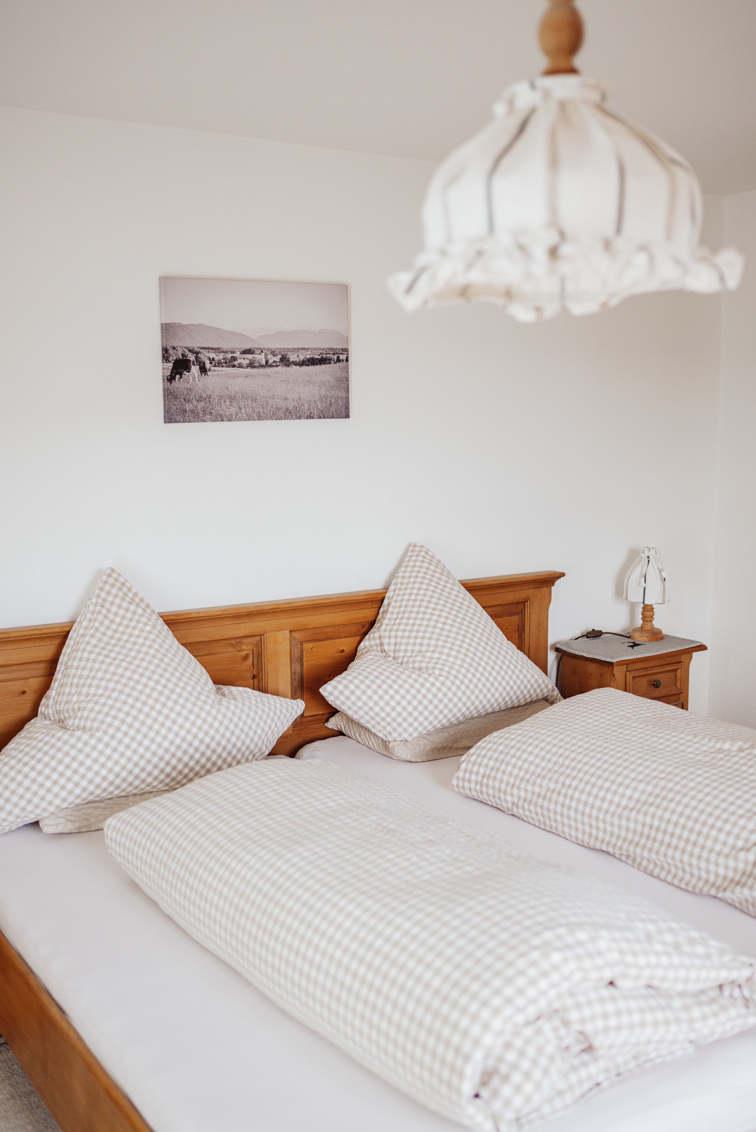 Un lit avec une tête de lit en bois, une literie à carreaux, une table de chevet avec une lampe et un tableau accroché au mur.