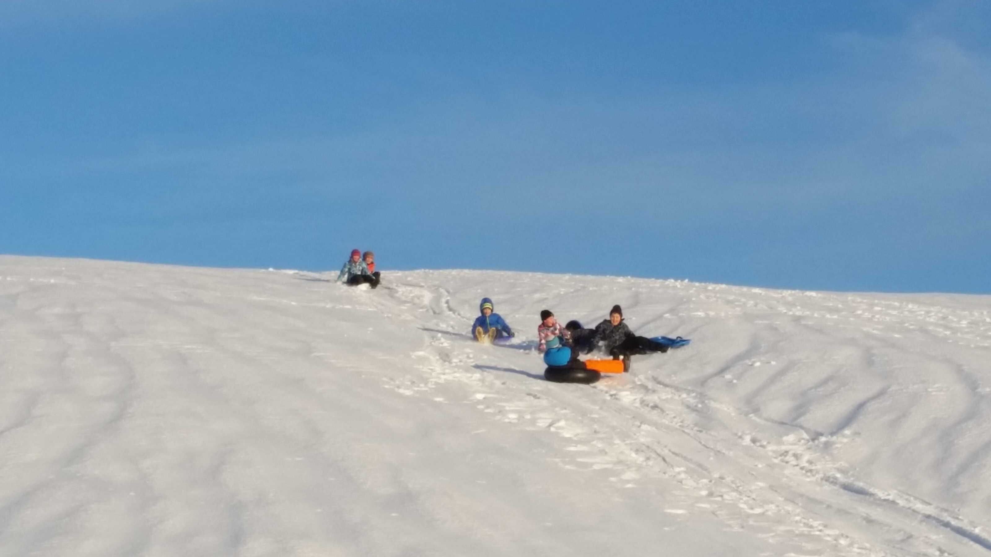 Een besneeuwde helling waar mensen sleeën.