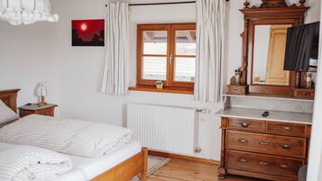 Une chambre à coucher comprenant un lit, une commode en bois, un miroir, une fenêtre avec des rideaux, un radiateur et un tableau accroché au mur.