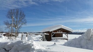 A wooden cabin with a snow-covered roof, surrounded by snow-covered ground and trees.