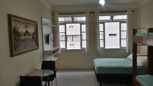 A room with bunk beds, a desk, a chair, a television, and a window with curtains. - Kitnet one block from Pitangueiras beach (Guarujá)