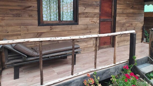 A wooden cabin with a porch, a bench, and a window with patterned curtains. - Las Cabañas Mongui (Monguí)