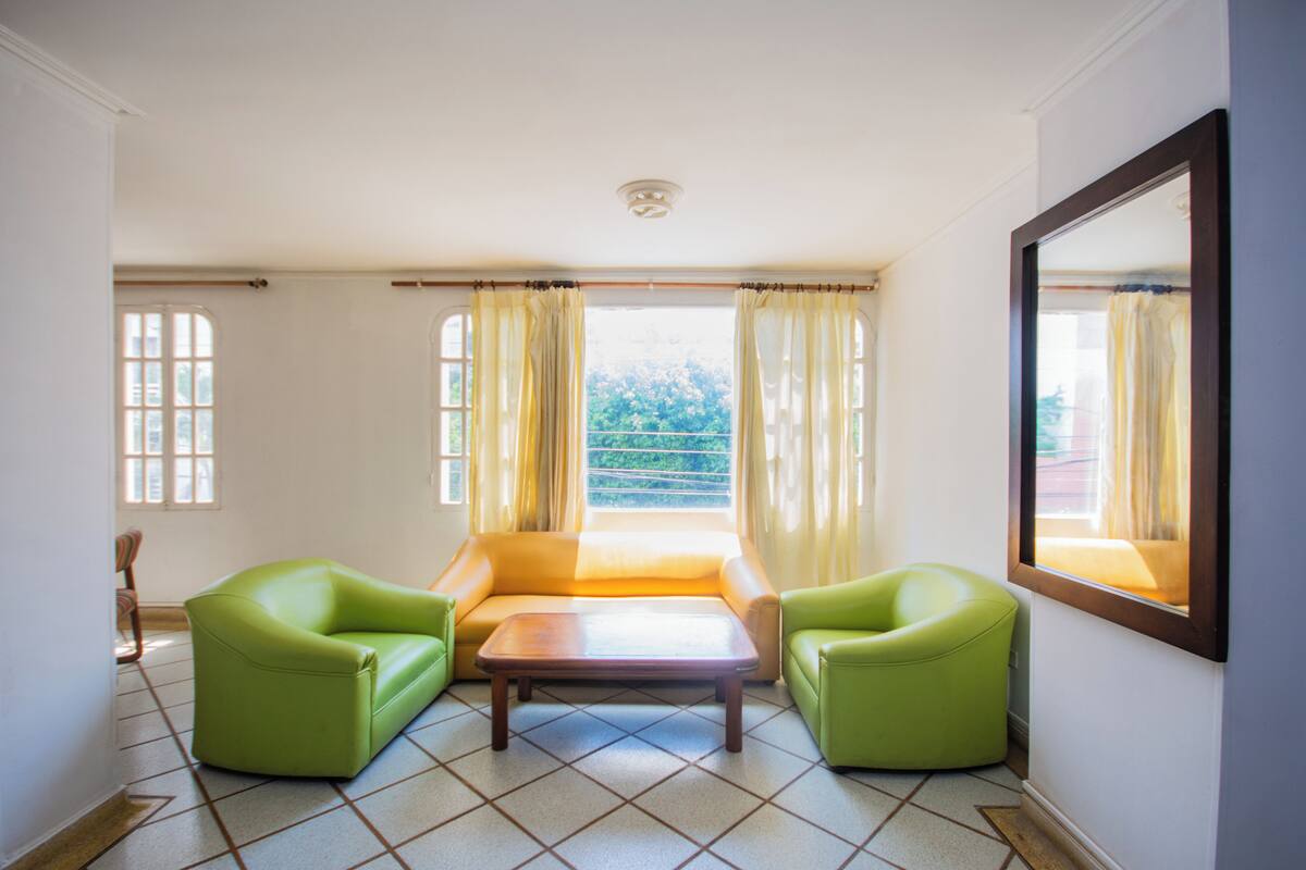 A room with a sofa, two armchairs, a coffee table, and a window with curtains.