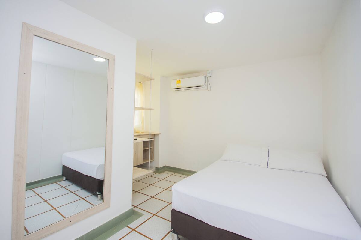 A bedroom with a bed, a mirror, a wardrobe, and an air conditioning unit.