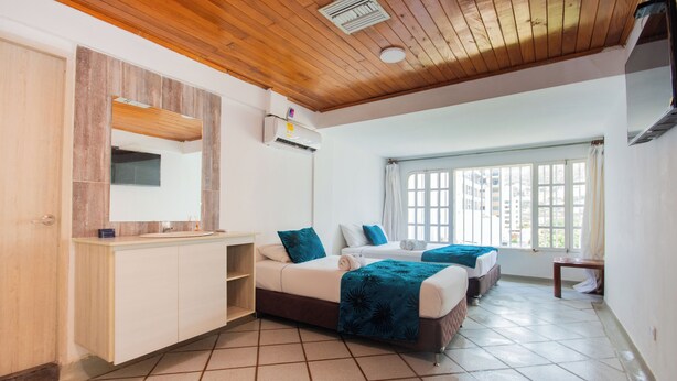 A hotel room with a wooden ceiling, a large window, a bed with a blue blanket, and a built-in wardrobe. - Hotel Sorrento Santa Marta (Santa Marta)