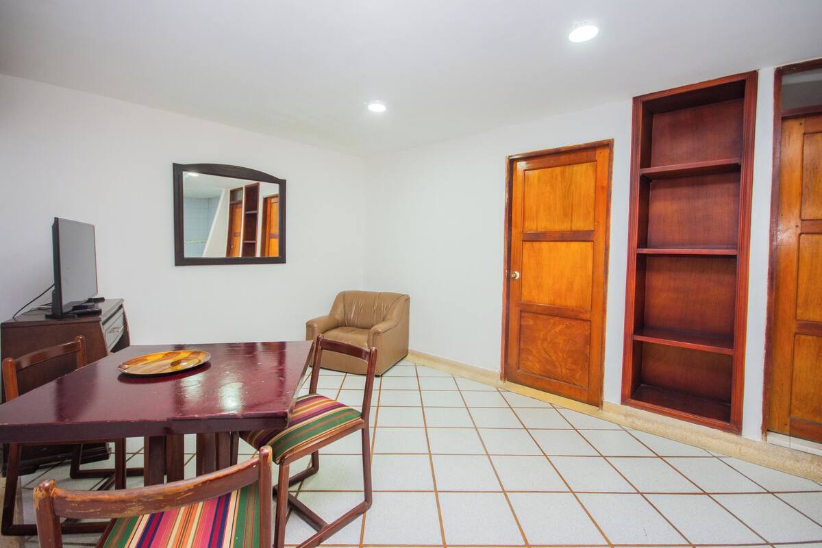 A dining area with a wooden table, chairs, a television, and a mirror on the wall.