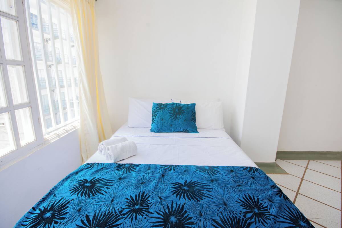 A single bed with a blue floral bedspread, white pillows, and a white blanket.