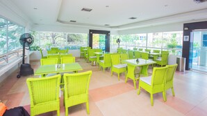 A bright indoor dining area with green chairs and tables, large windows, and a fan. - Hotel Sorrento Santa Marta (Santa Marta)
