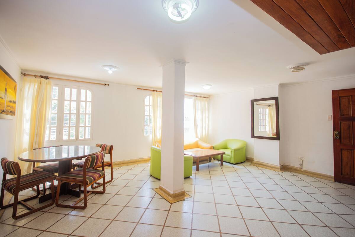 A dining area with a round table and chairs, a green sofa, and a wooden ceiling.