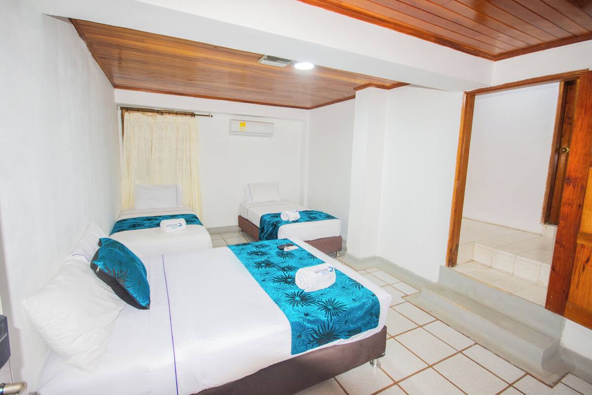 A hotel room with two beds, wooden ceiling, white walls, and a wooden door.