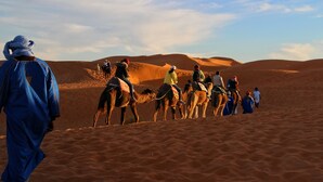A group of people riding camels across a desert landscape. - Dar Marhaba (Taouz)