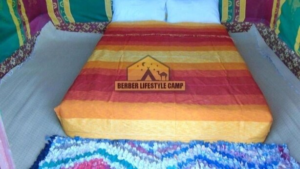 A bed with a colorful striped blanket and a headboard with camel designs. - Dar Marhaba (Taouz)