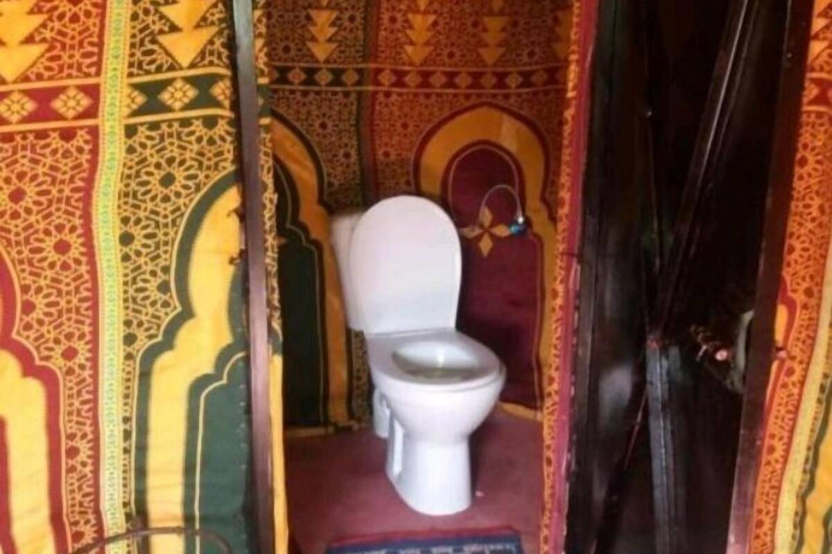 A small, narrow room with a toilet, a metal chair, and a patterned mat on the floor.
