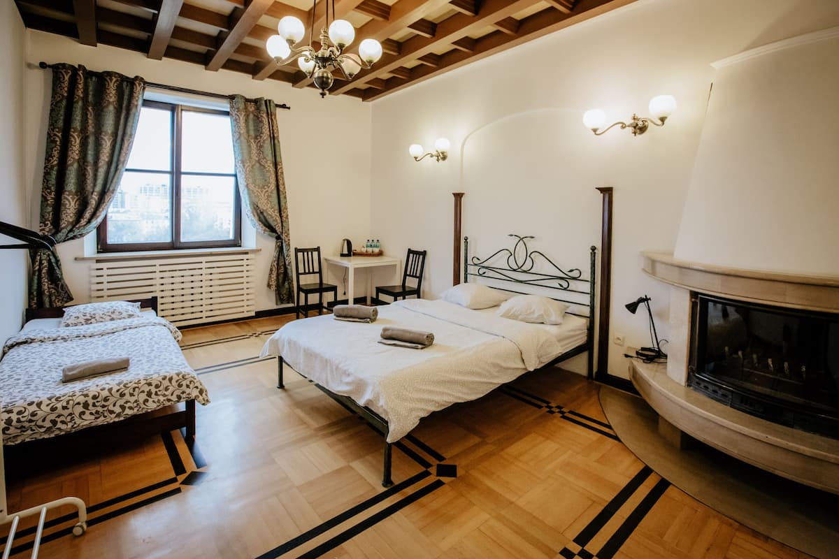 A bedroom with a bed, a chair, a table, a fireplace, and a window with curtains.