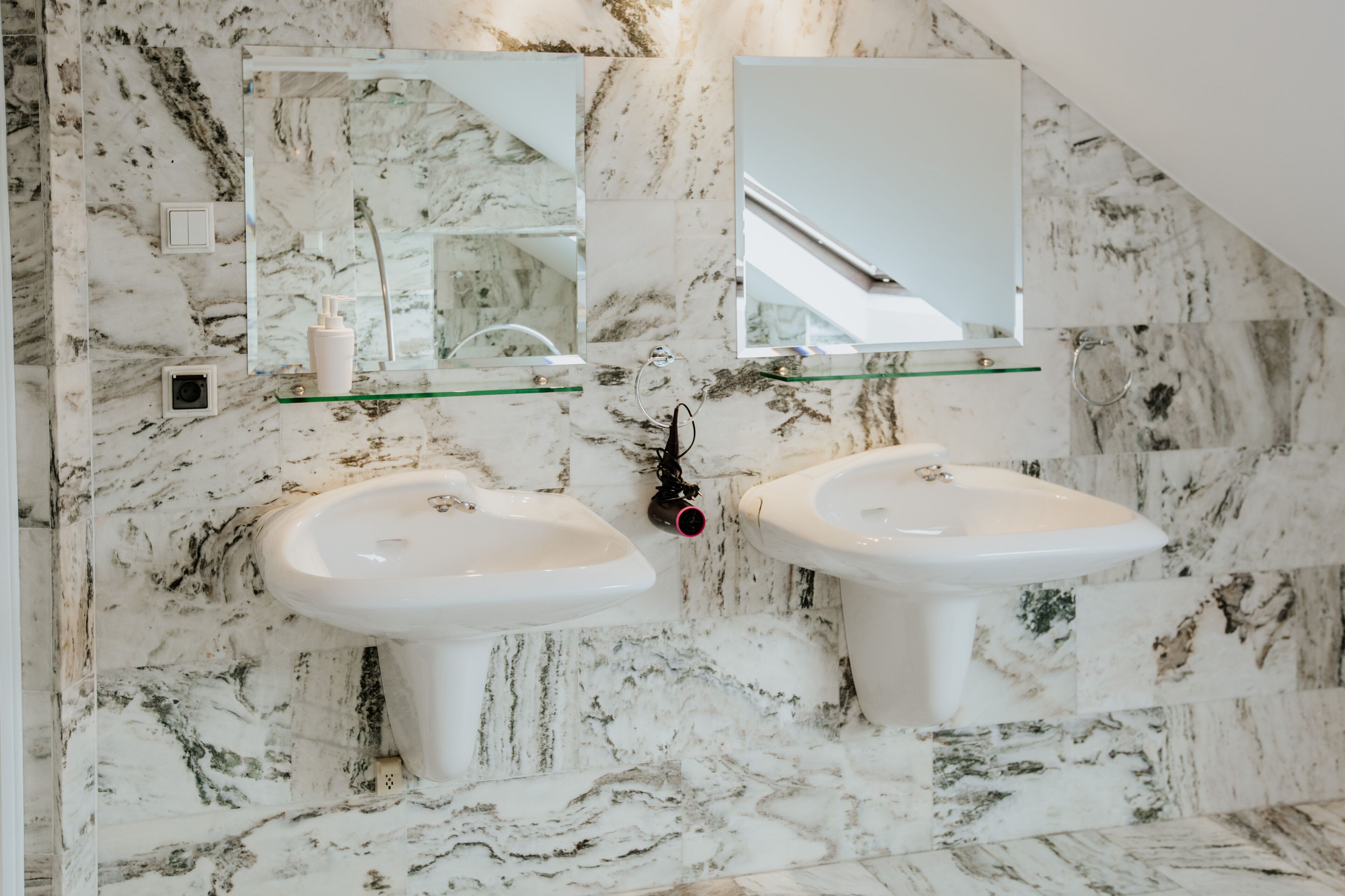 A bathroom with two sinks, a glass shelf, a mirror, and marble walls.
