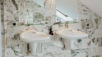 A bathroom with two sinks, a glass shelf, a mirror, and marble walls.