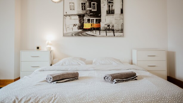 Habitación de hotel con una cama, dos mesitas de noche, una lámpara de pared y un cuadro con una escena callejera.
