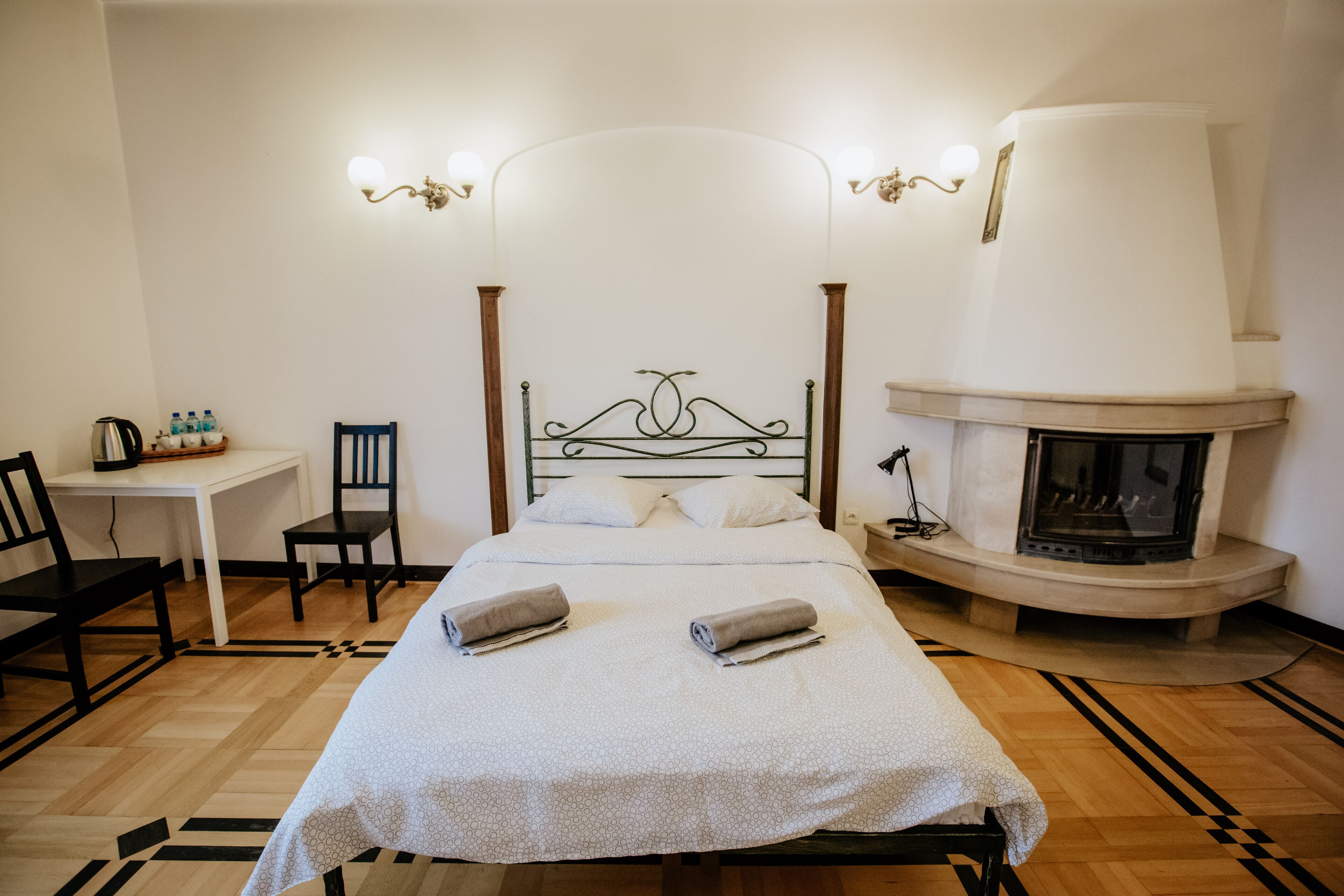 A neatly arranged bedroom with a bed, a desk, chairs, and a fireplace.
