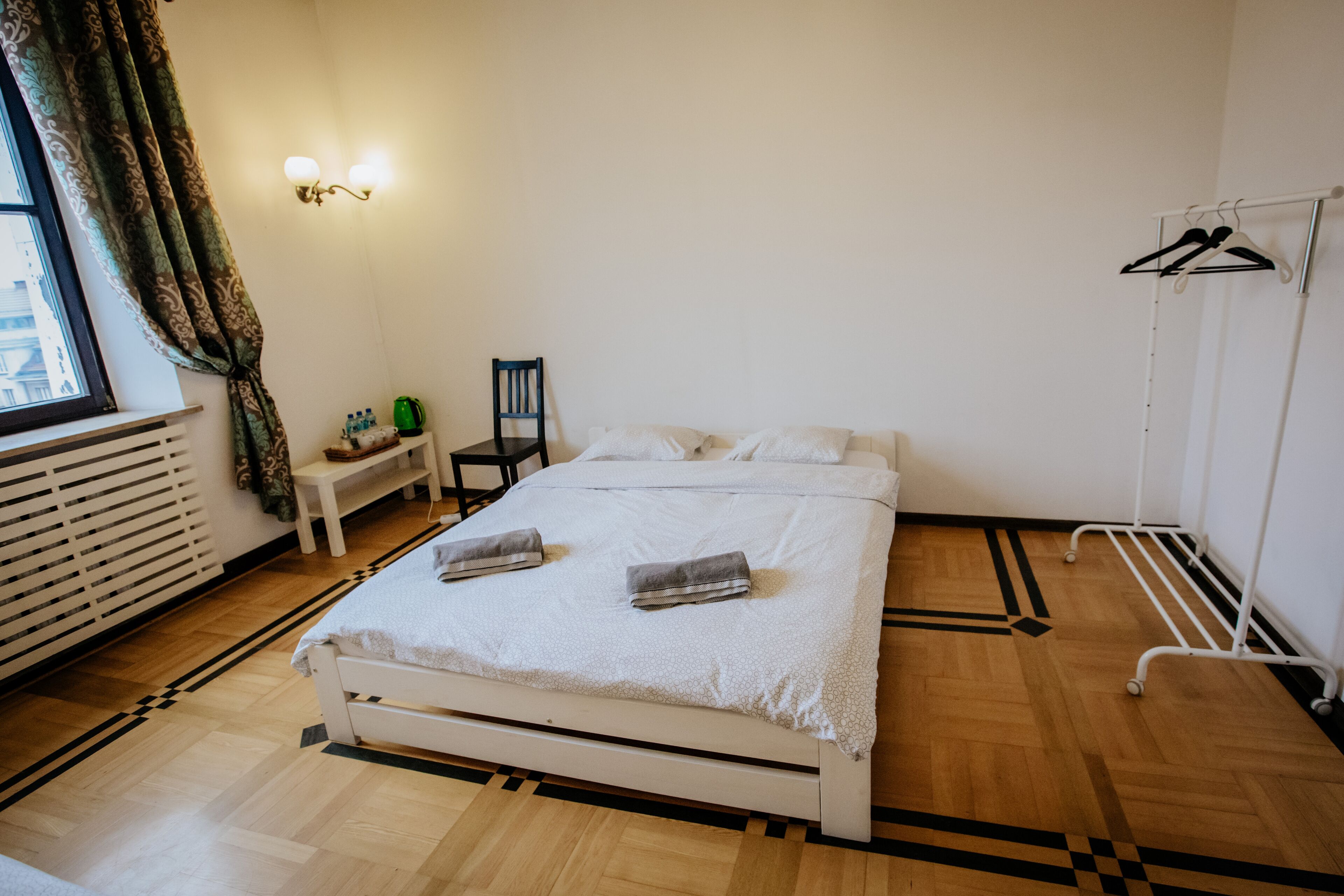 A neatly arranged bedroom with a bed, bedside table, chair, and a clothing rack.