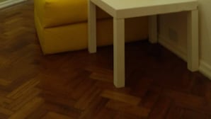 A corner room with a yellow sofa and a small white table.