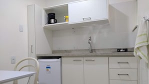 A compact kitchenette with a refrigerator, a coffee maker, and a small shelf.