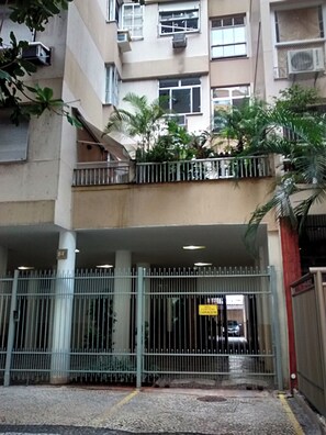 Un edificio residencial de varios pisos con entrada protegida, balcones y unidades de aire acondicionado.