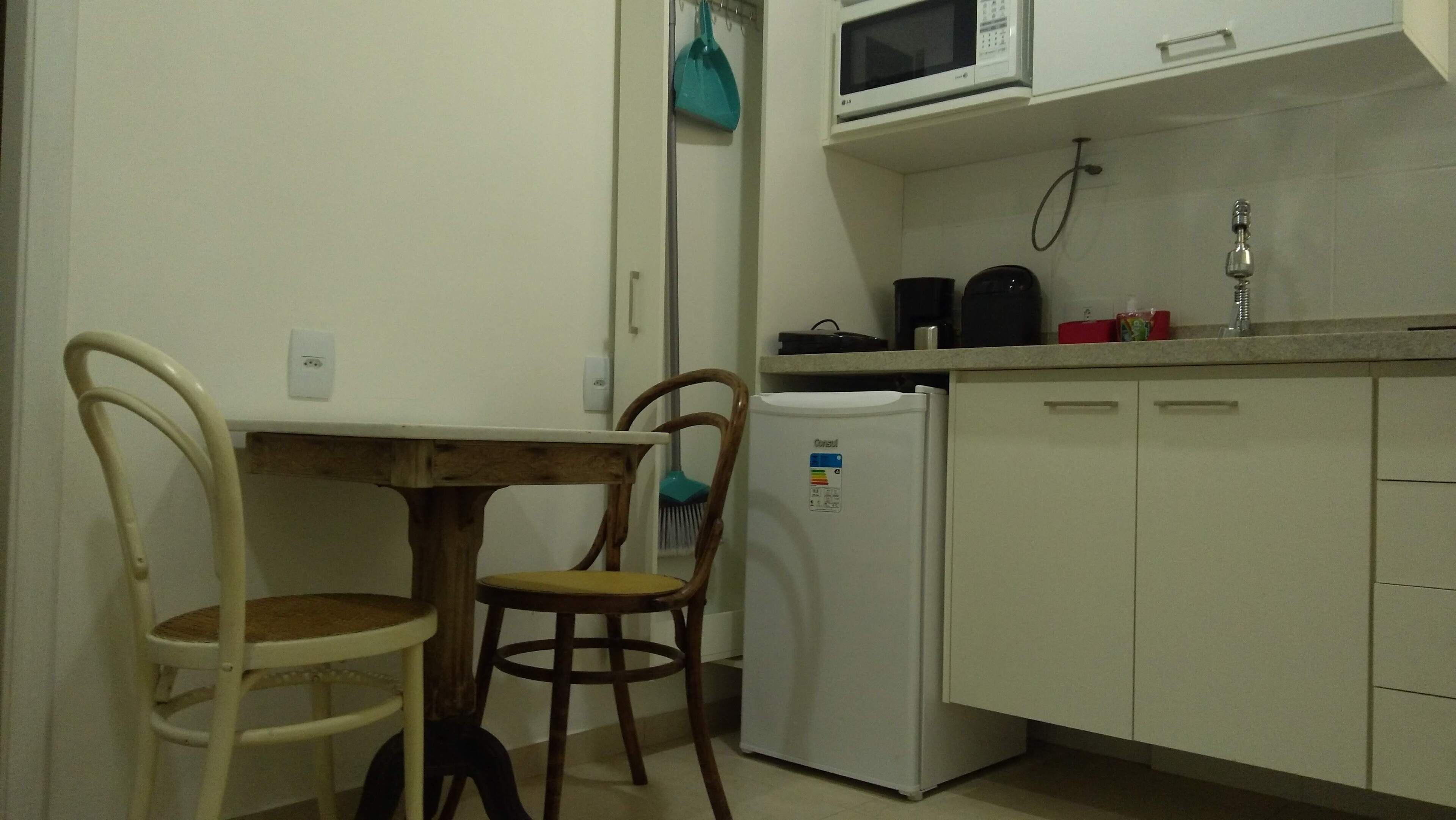 A compact kitchen with a white refrigerator, a microwave, and a sink. There is a wooden table with two chairs.