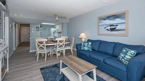 Una sala de estar con un sofá azul, una mesa de centro de madera y un comedor con mesa y sillas.