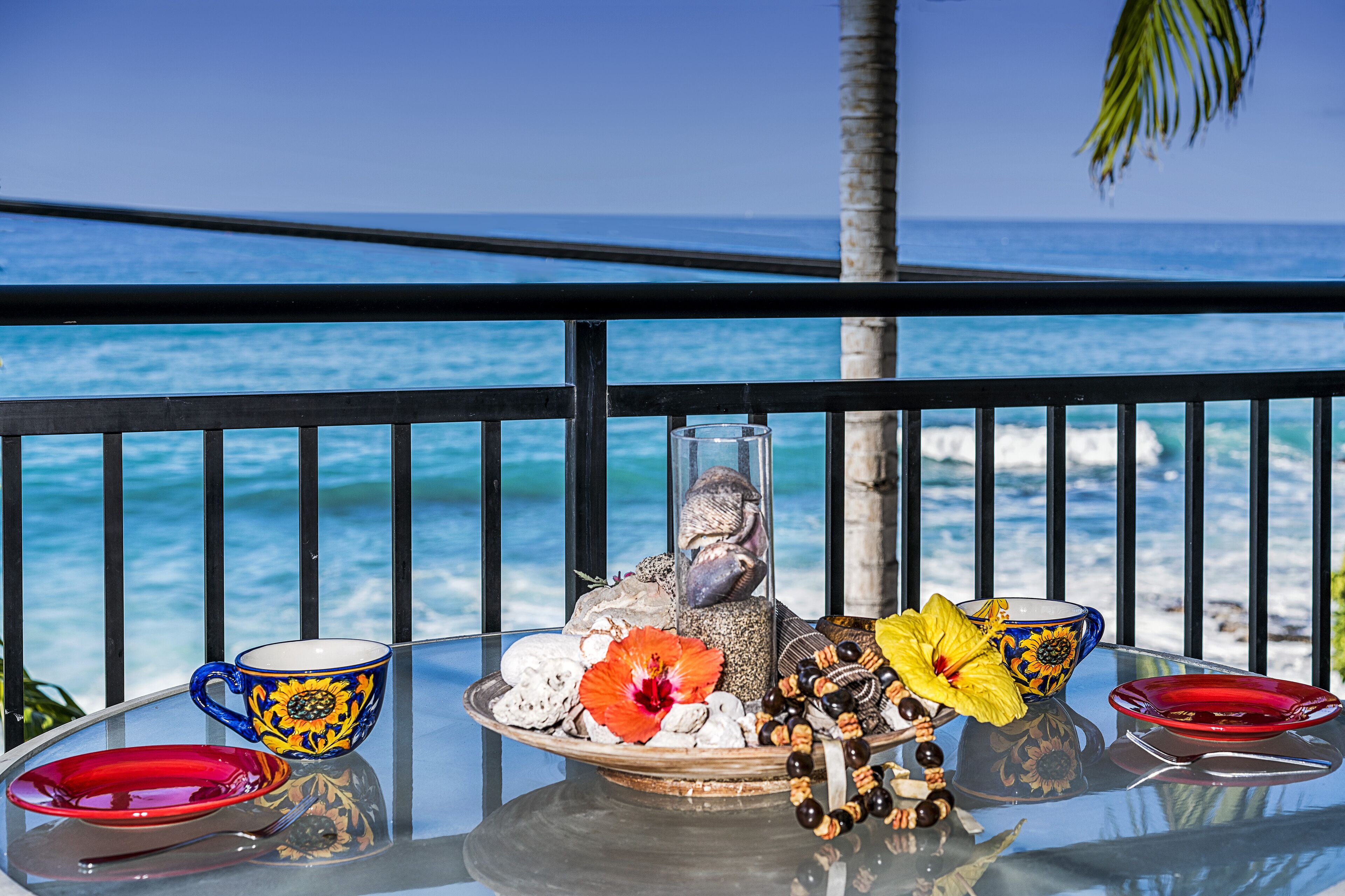 A table with a glass vase, a bowl, and a plate with decorative items, set against a view of the ocean.