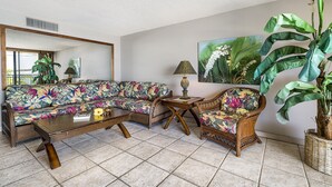 Una sala de estar con sofá, sillón, mesa de centro y una planta grande en maceta.