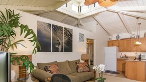 A spacious living area with a sofa, a round wicker coffee table, and a dining table. There is a kitchen in the background with wooden cabinets and a refrigerator. - Private Guest Suite near Beaches, Hiking & Golfing (Princeville)