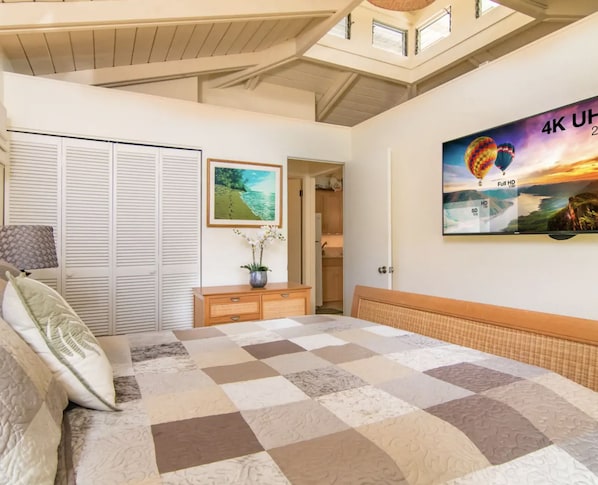 Een slaapkamer met een groot bed, een garderobe, een nachtkastje met een vaas, en een schilderij van een luchtballon.