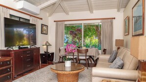 A living room with a TV, a wicker coffee table, a sofa, and a dining area with a table and chairs. - Private Guest Suite near Beaches, Hiking & Golfing (Princeville)