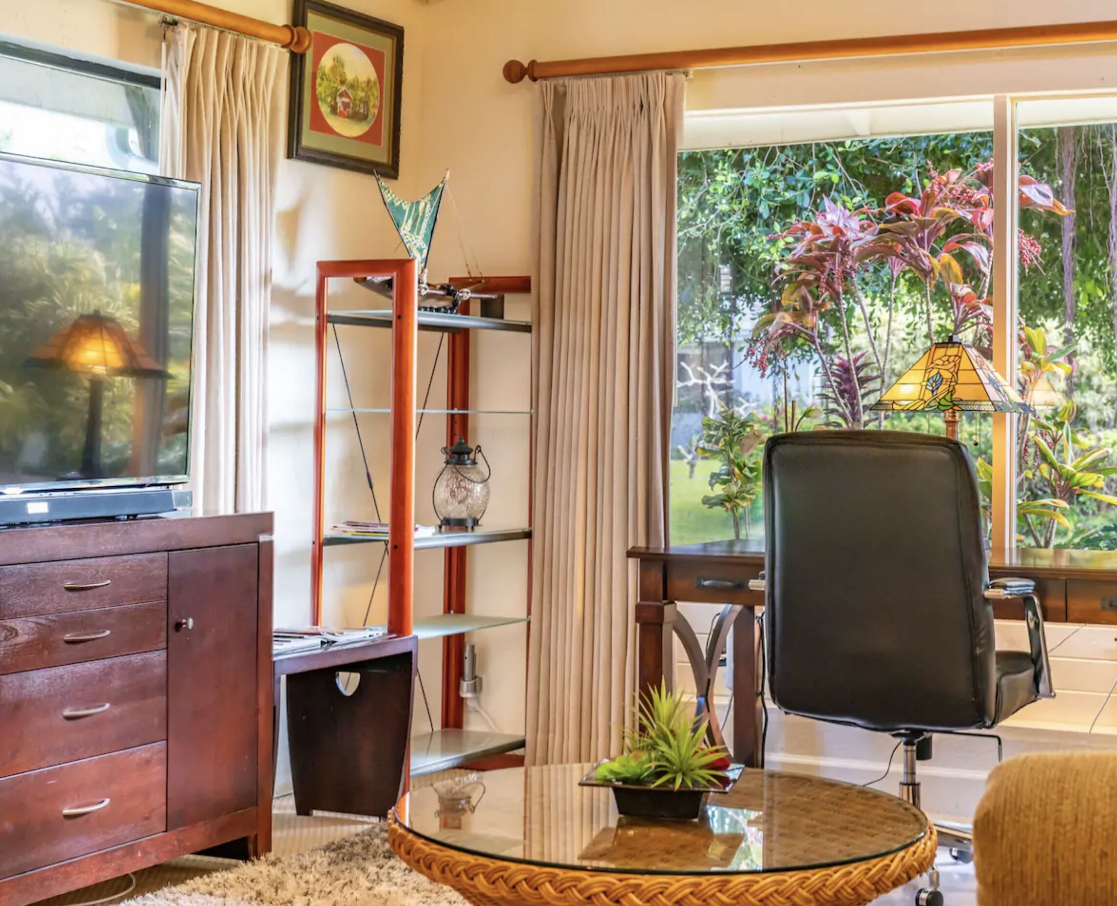 Una habitación con un armario de madera, una mesa de vidrio con una planta, una silla y vistas al verdor exterior.
