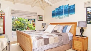 A bedroom with a bed, bedside tables, a lamp, a window with a view of greenery, and a ceiling fan. - Private Guest Suite near Beaches, Hiking & Golfing (Princeville)