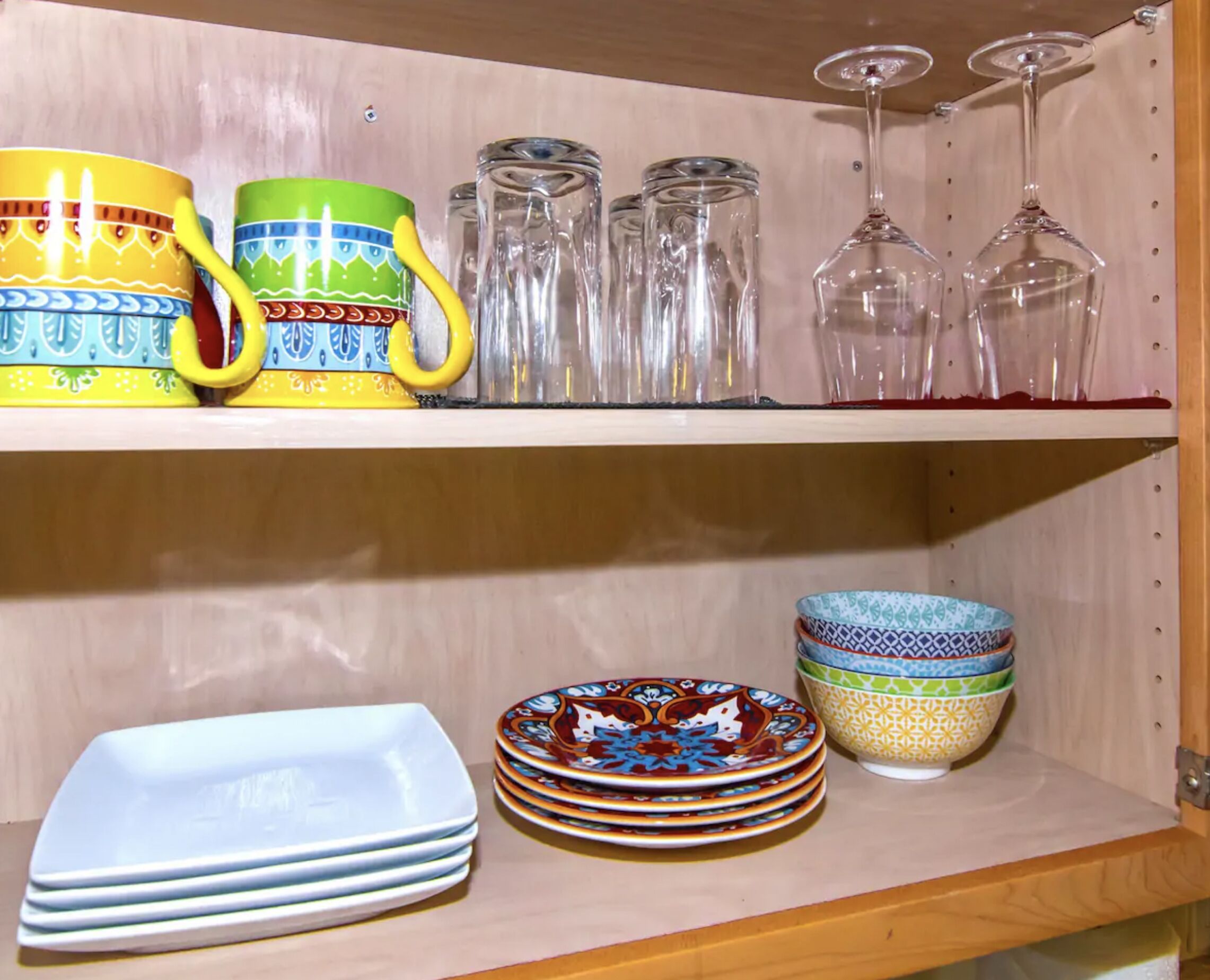 A shelf with colorful mugs, clear glasses, and decorative plates.