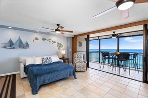 Relax in this serene ocean-view room featuring a large bed, nightstand, and ceiling fan.