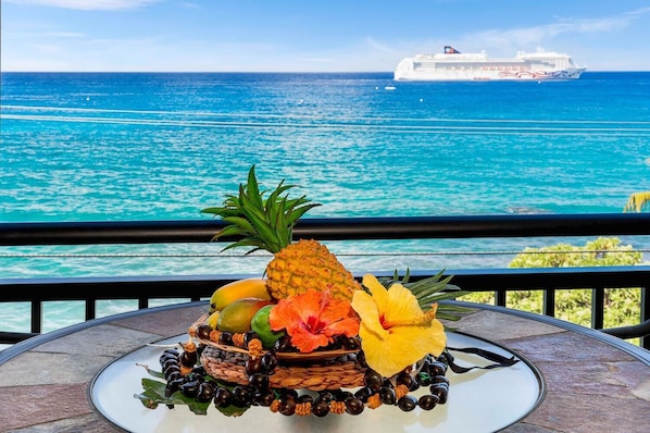 Enjoy breathtaking ocean views from this balcony, where a beautiful fruit and flower arrangement awaits.
