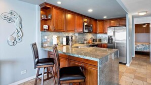 Cocina moderna con armarios de madera, encimera de granito, electrodomésticos de acero inoxidable y una pieza decorativa de un caballito de mar en la pared.