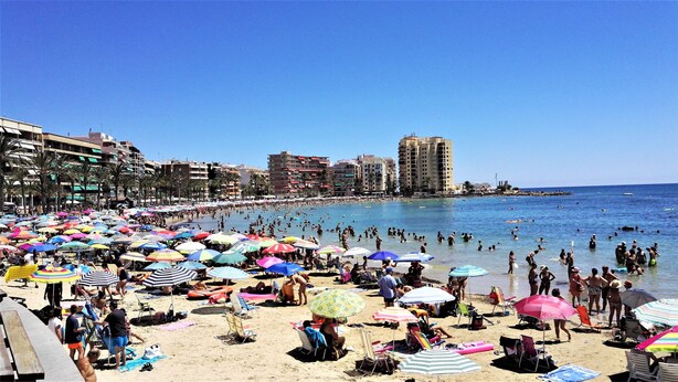 A crowded beach with numerous umbrellas and people enjoying the water.