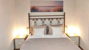 A neatly made bed with a headboard, two bedside tables with lamps, and a painting above the bed.
