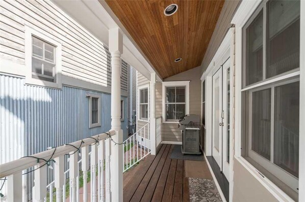 A covered porch with a wooden ceiling, white railings, and a small outdoor utility area.