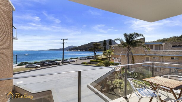 Un balcon avec vue sur la mer, des voitures garées et un immeuble à la façade en briques.