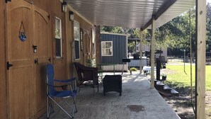 A covered outdoor area with wooden walls, a blue folding chair, a small table, and a metal grill.