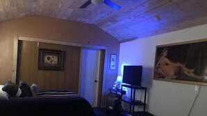 A bedroom with a bed, a desk with a computer, a ceiling fan, and a door.