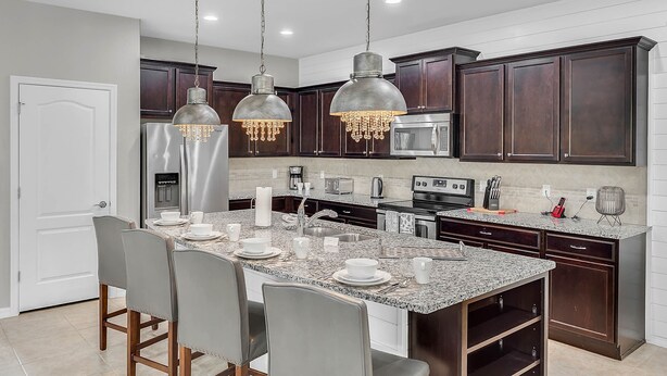 A modern kitchen with granite countertops, dark wooden cabinets, stainless steel appliances, and pendant lighting.
