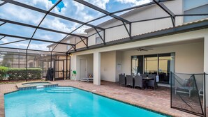 A swimming pool with a glass enclosure, outdoor seating, and a covered patio area.