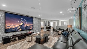 A modern living room with a large flat-screen TV, a leather sofa, a coffee table, and a stone wall.
